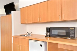 Cocina compacta con muebles de madera, microondas, cafetera y lavavajillas.