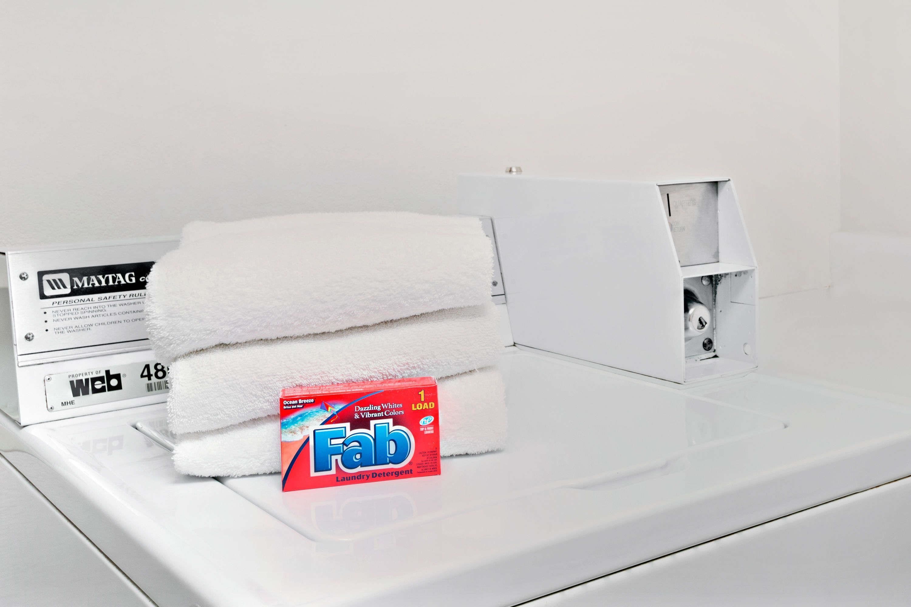 A white washing machine with a folded white towel and a box of Fab laundry detergent.