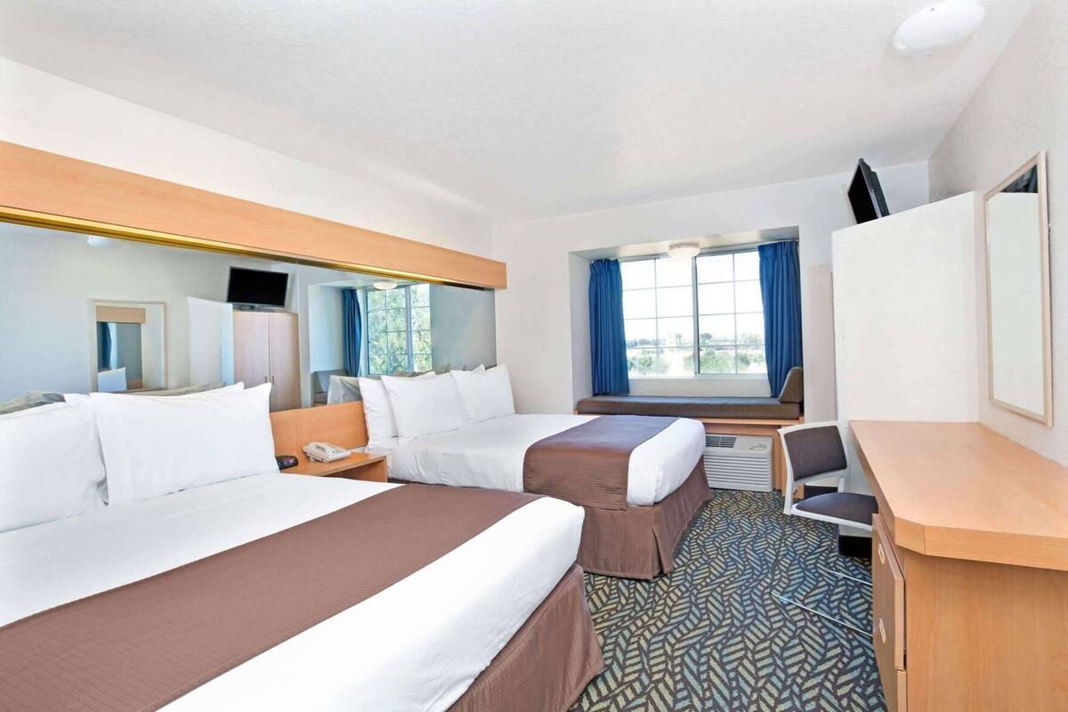 Une chambre d’hôtel avec deux lits, un bureau, une chaise, une télévision et une fenêtre avec des rideaux.