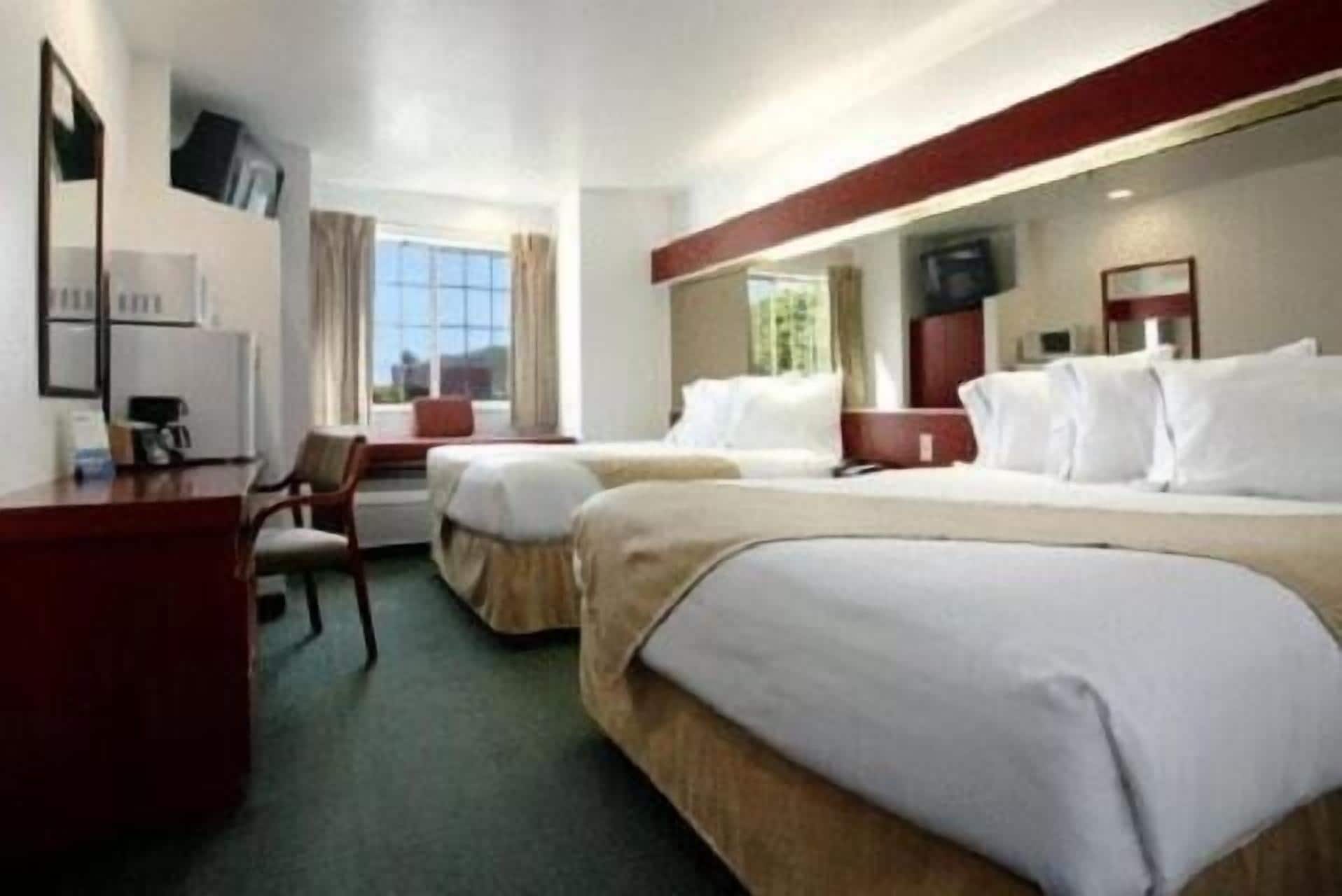 Une chambre d’hôtel avec deux lits, un bureau, une chaise, une télévision et une fenêtre avec des rideaux.