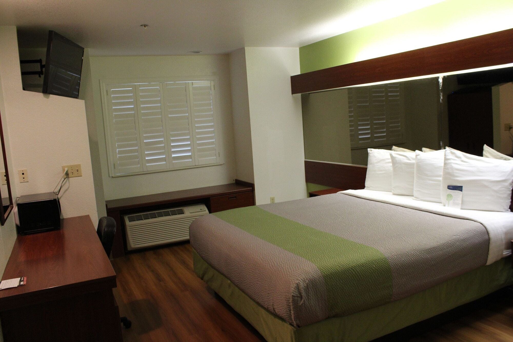 A hotel room with a bed, a desk, a chair, a television, and a window with blinds.