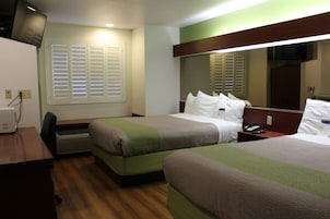 Habitación de hotel con dos camas, un escritorio y un espejo grande.