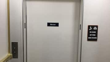 Een liftdeur met een bordje waarop staat 'lift' en een ander bordje dat adviseert de trap te gebruiken in geval van brand.