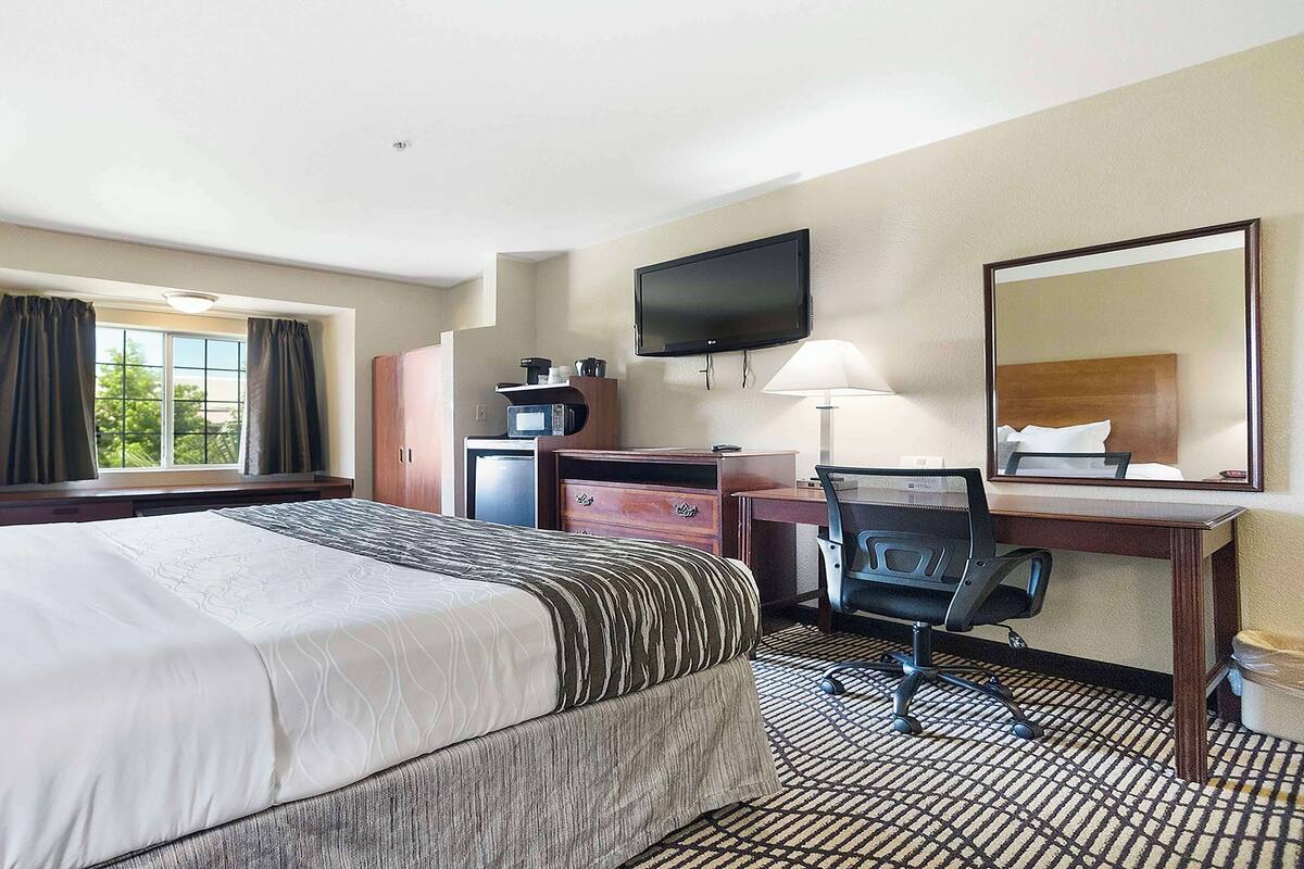 Een hotelkamer met een groot bed, een bureau met stoel, een televisie en een raam met gordijnen.