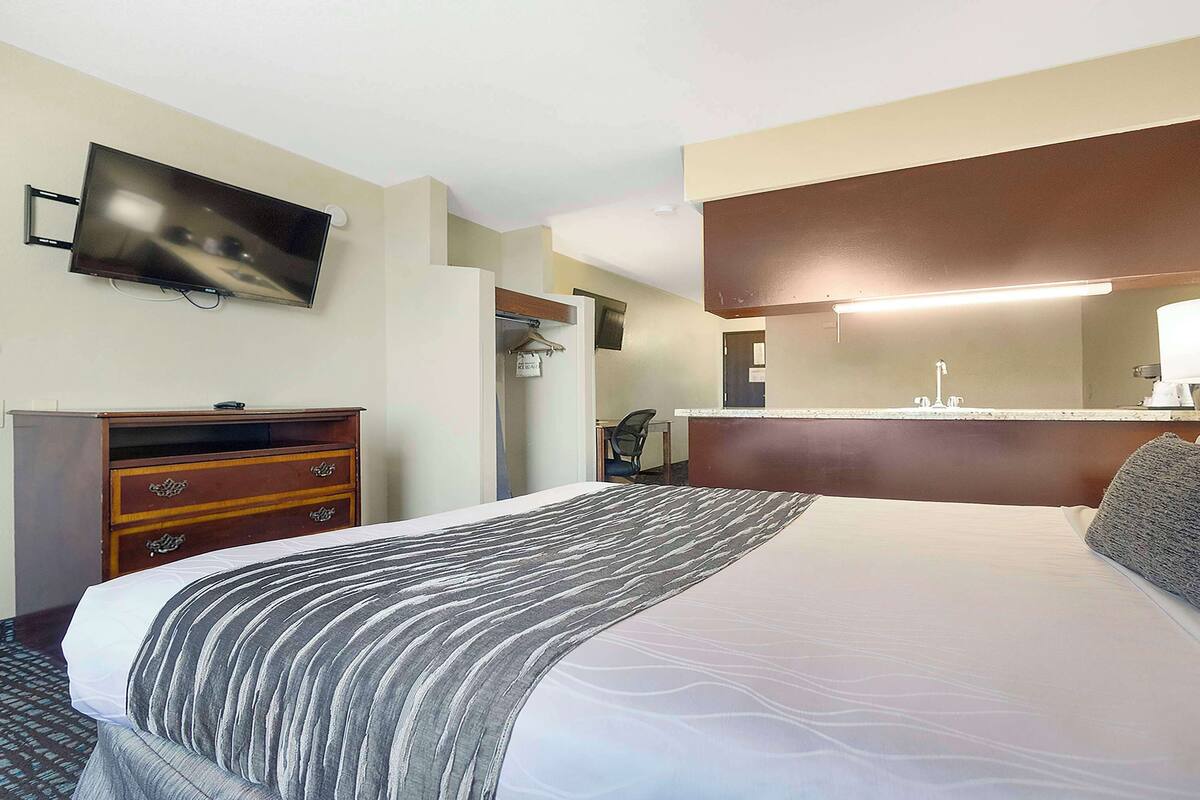 Een hotelkamer met een bed, een dressoir, een aan de muur bevestigde televisie, een spiegel en een bedlamp.