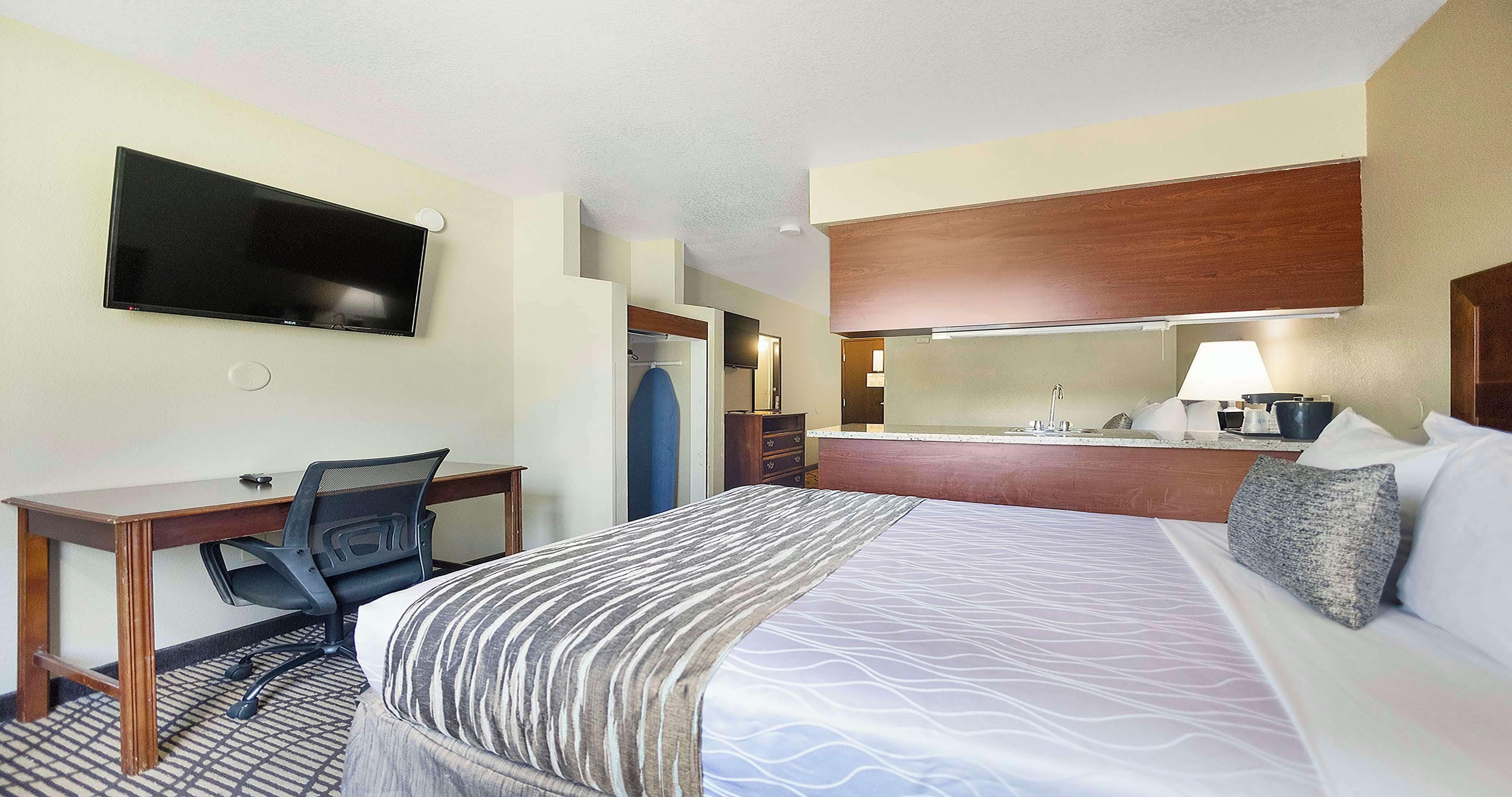 Une chambre d’hôtel équipée d’un lit, d’un bureau, d’une chaise, d’une télévision et d’un coin cuisine.
