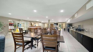 Un grand espace de salle à manger avec plusieurs tables et chaises, un coin cuisine équipé d’appareils modernes et un panneau indiquant la sortie.