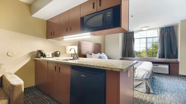 Une chambre d’hôtel compacte dotée d’une kitchenette, comprenant un four à micro-ondes, un évier et un petit réfrigérateur. La chambre dispose d’un lit et offre une vue sur l’extérieur grâce à une fenêtre.