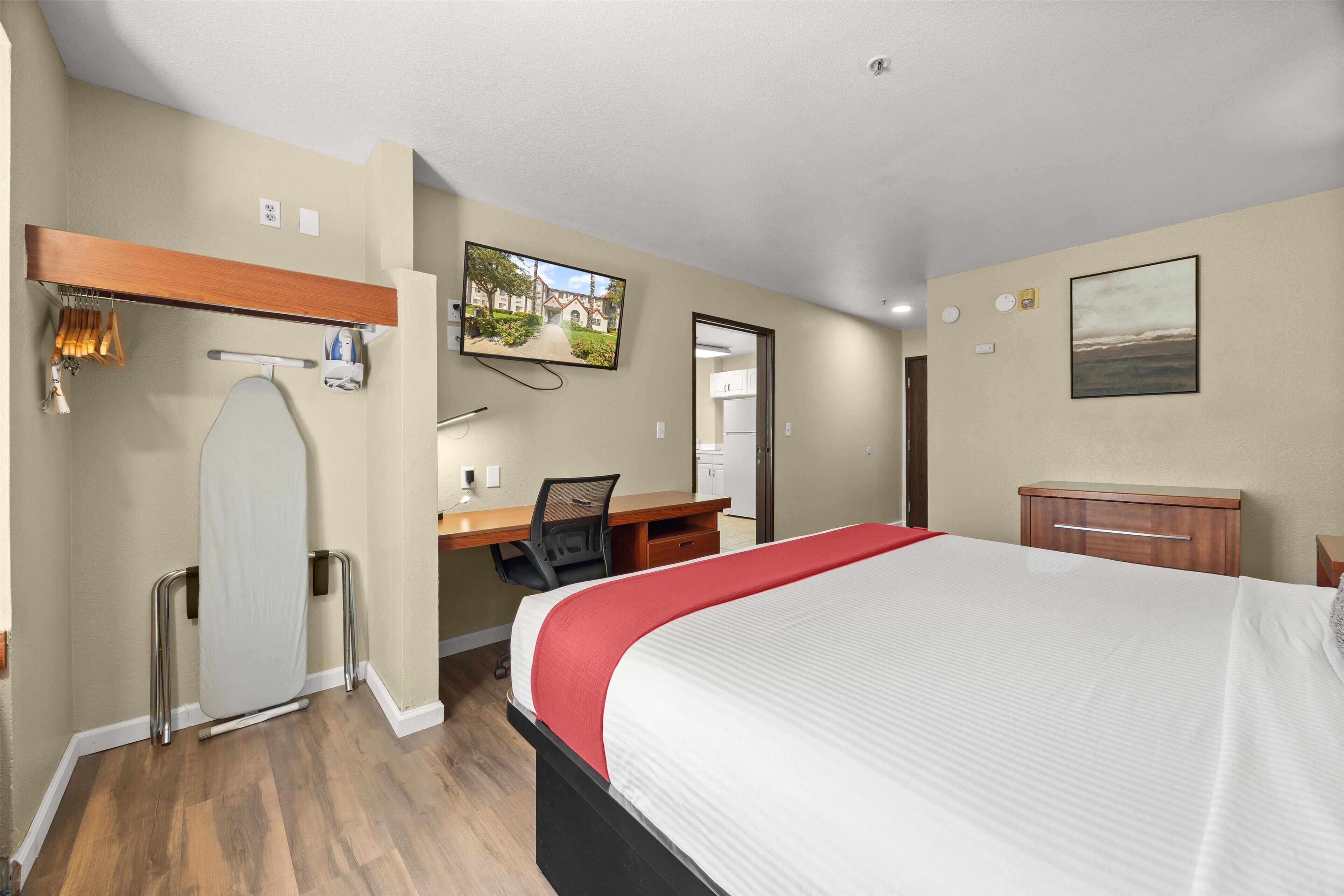 Una habitación de hotel con cama, escritorio, silla y televisor en la pared.