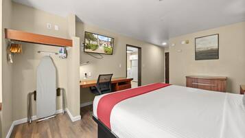 Una habitación de hotel con cama, escritorio, silla y televisor en la pared.
