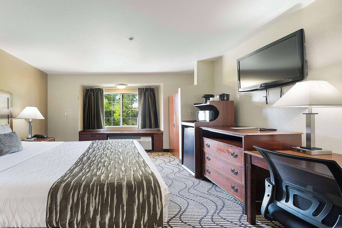 Een hotelkamer met een groot bed, een bureau, een stoel, een televisie en een raam met gordijnen.