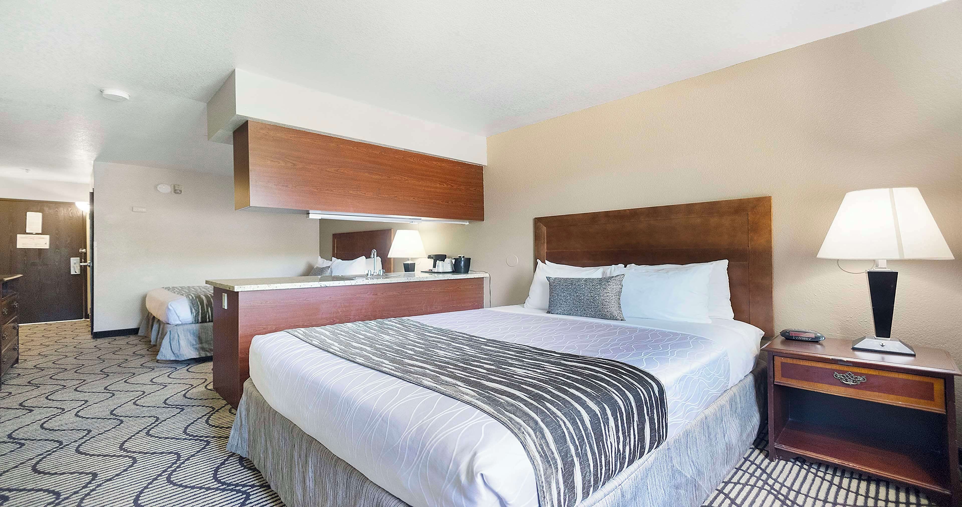 Une chambre d’hôtel avec un grand lit, une tête de lit en bois, une table de chevet avec une lampe et un bureau doté d’un miroir et d’une machine à café.