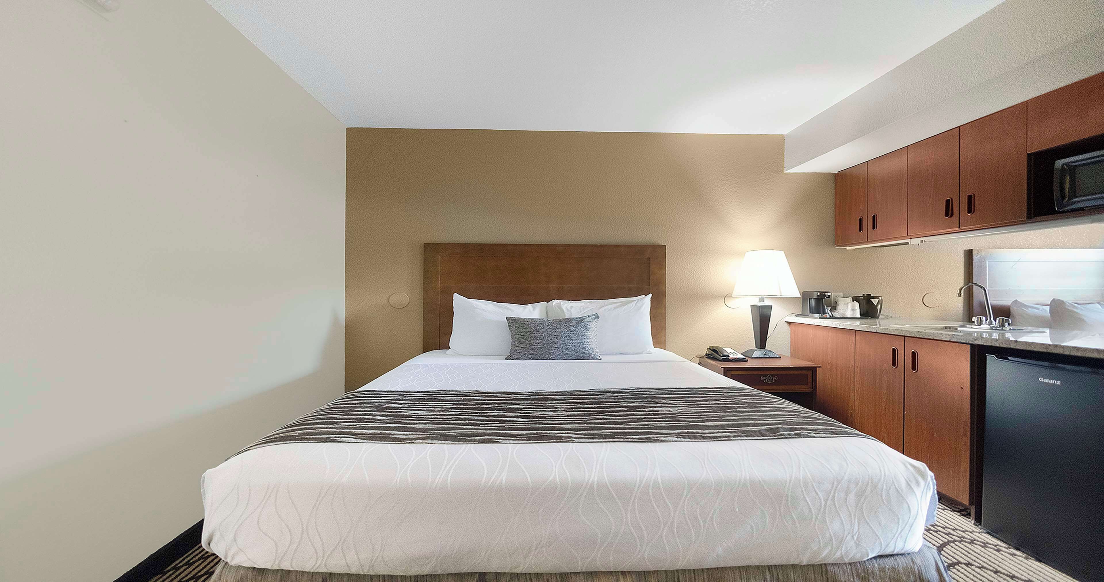 Habitación de hotel con cama, lámpara de noche, microondas y una pequeña cocina.