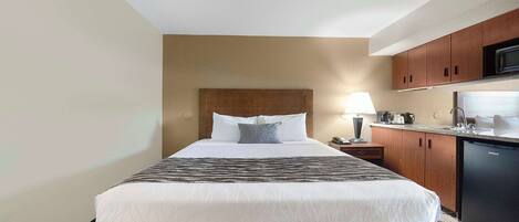 A hotel room with a bed, a bedside lamp, a microwave, and a small kitchenette.