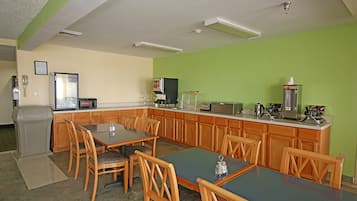 Una cocina con armarios de madera, una mesa de comedor y sillas. Hay un microondas, una cafetera y un cubo de basura.
