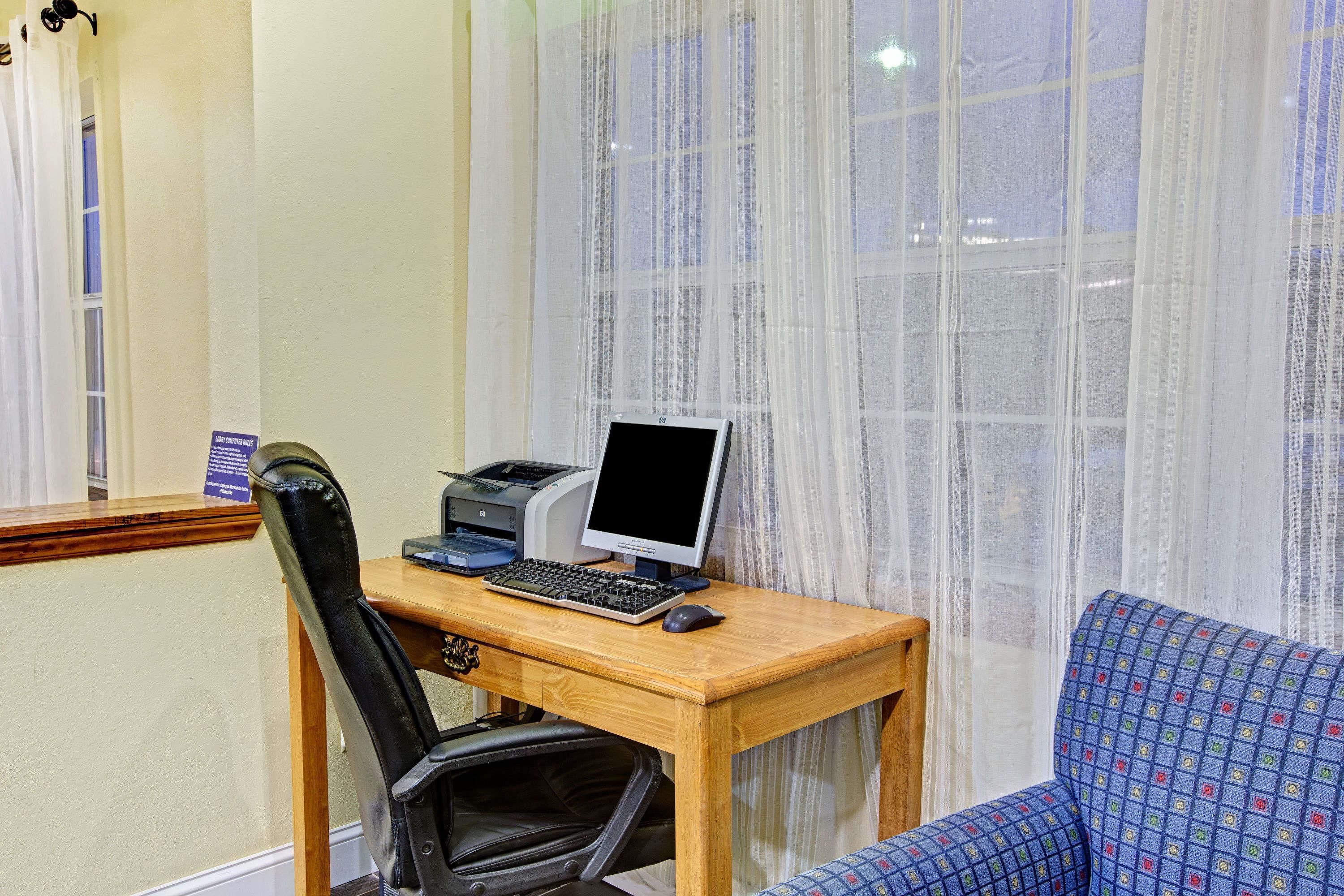 Et værelse med skrivebord i træ, en computer, en printer, en sort stol og en blå sofa med mønster.
