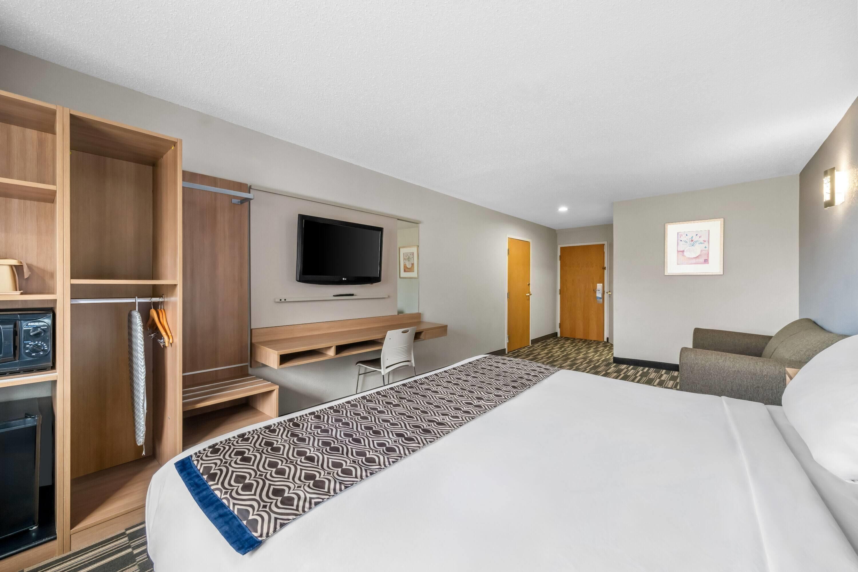 A hotel room with a bed, a desk, a television, a wardrobe, and a seating area.
