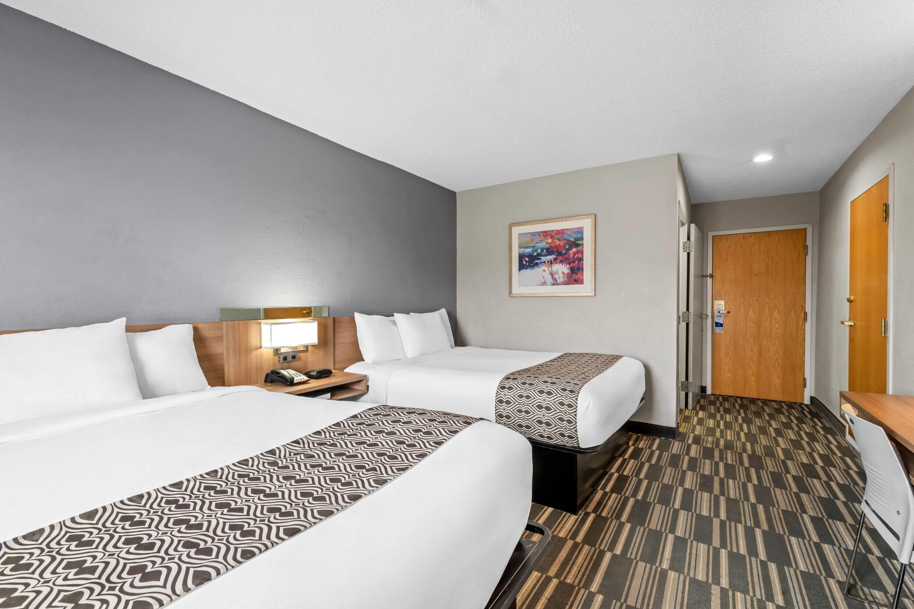 A hotel room with two beds, a desk, a chair, a lamp, and a painting on the wall.