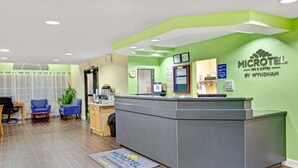 Un área de recepción con un mostrador gris, una pared verde con el logotipo de Microtel, un reloj y un calendario.