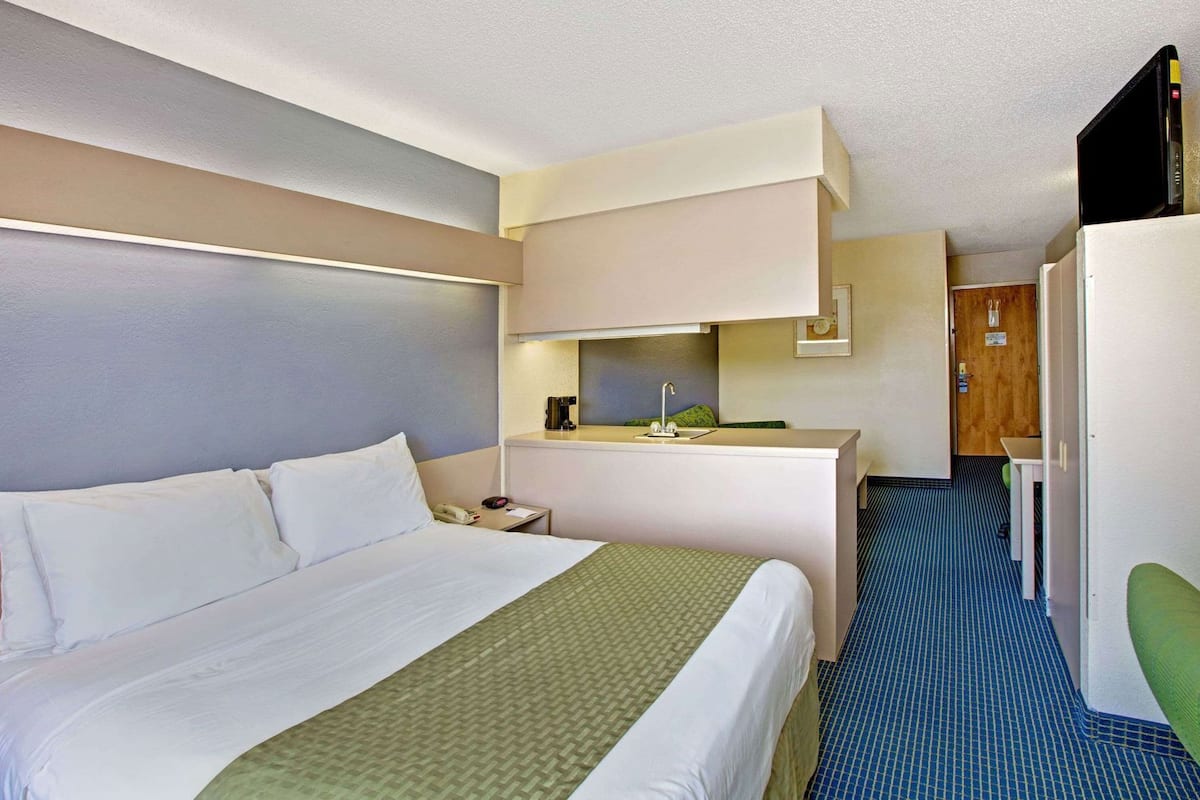 A hotel room with a bed, a desk, a sink, and a door.