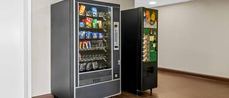 Een automaat met snacks en dranken, een drukknoop en een groene machine met een drankdispenser.