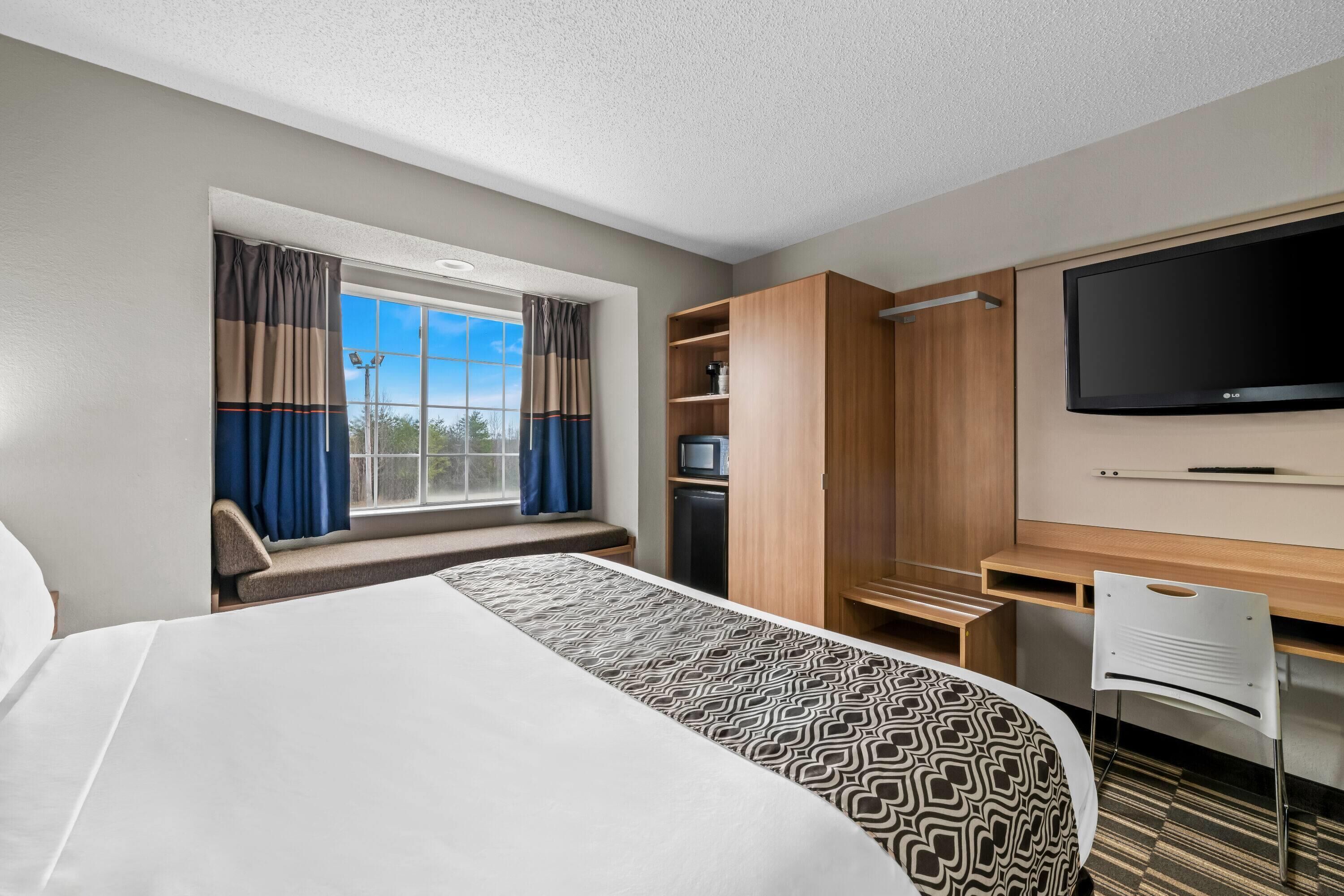 A hotel room with a large bed, a desk with a flat-screen TV, a wardrobe, and a window with curtains.