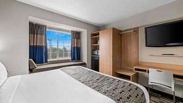 A hotel room with a large bed, a desk with a flat-screen TV, a wardrobe, and a window with curtains.