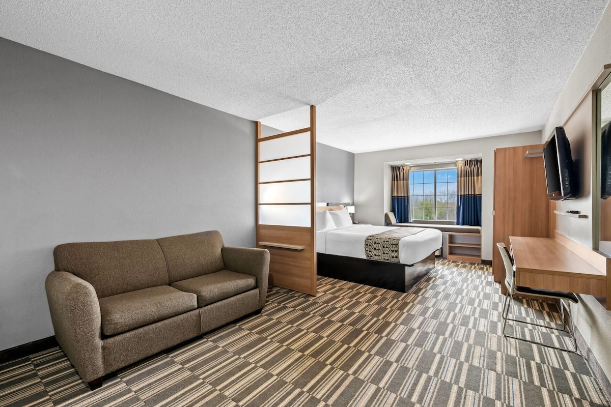 A hotel room with a sofa, a bed, a desk, a TV, and a window with curtains.