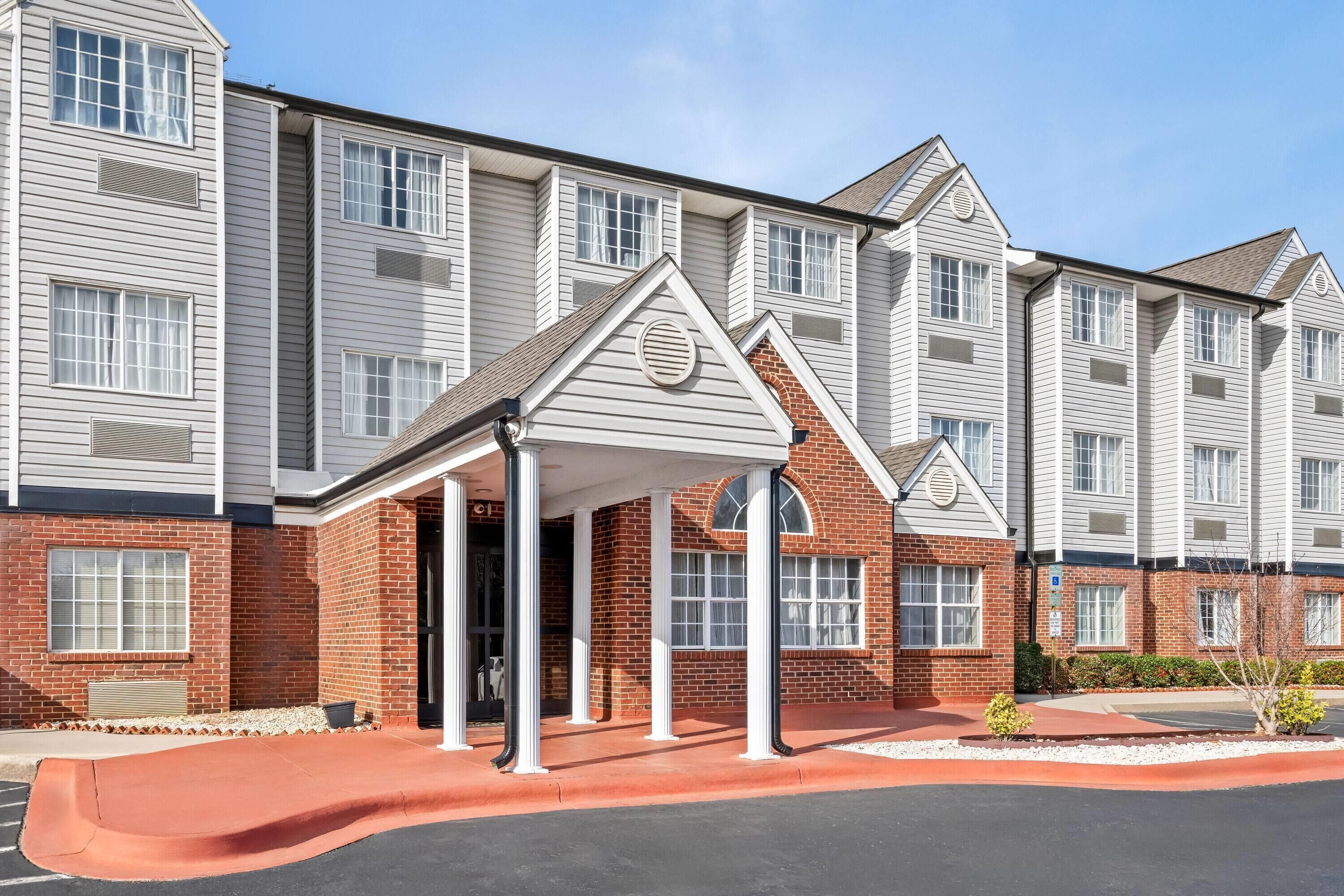 A multi-story hotel with a covered entrance, brick facade, and a parking area.