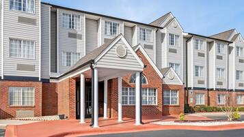 A multi-story hotel with a covered entrance, brick facade, and a parking area.