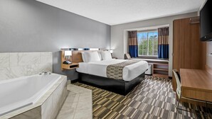 Habitación de hotel con una cama grande, baño independiente con bañera, escritorio y televisor.