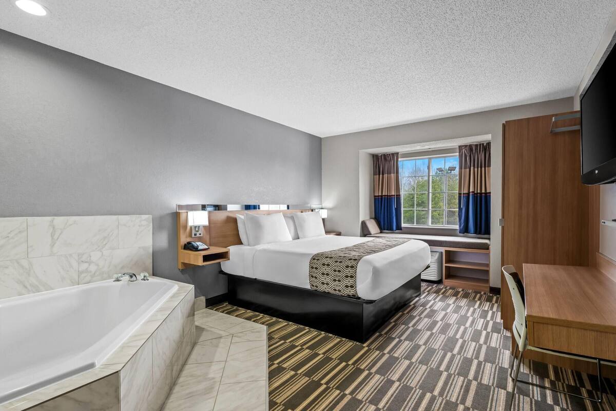 A hotel room with a large bed, a separate bathroom with a bathtub, a desk, and a TV.