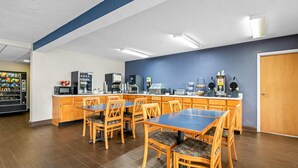 Una cocina moderna con armarios de madera, microondas y cafetera. Hay varias mesas y sillas de madera.