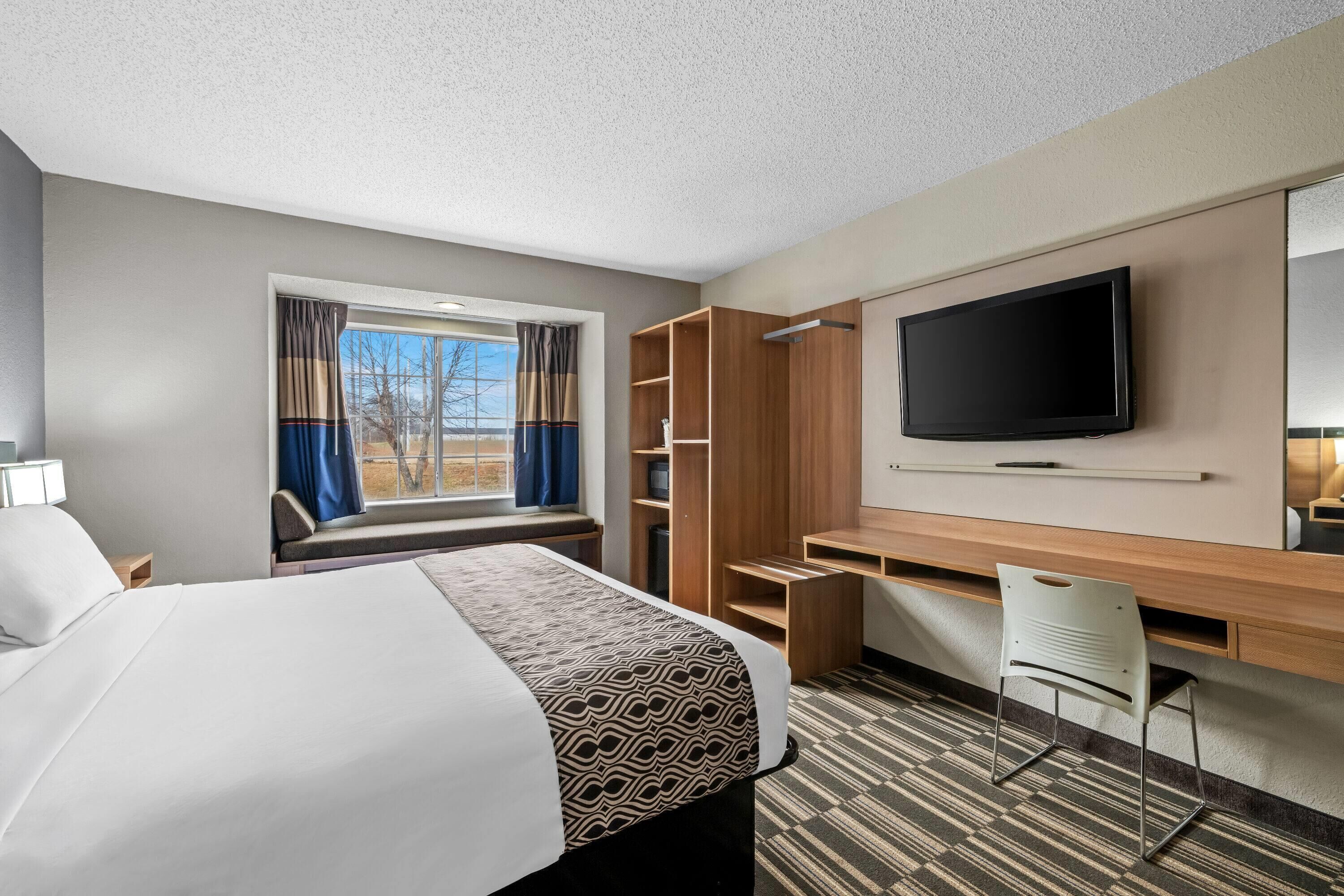 A hotel room with a large bed, a desk with a chair, a TV, and a window with curtains.
