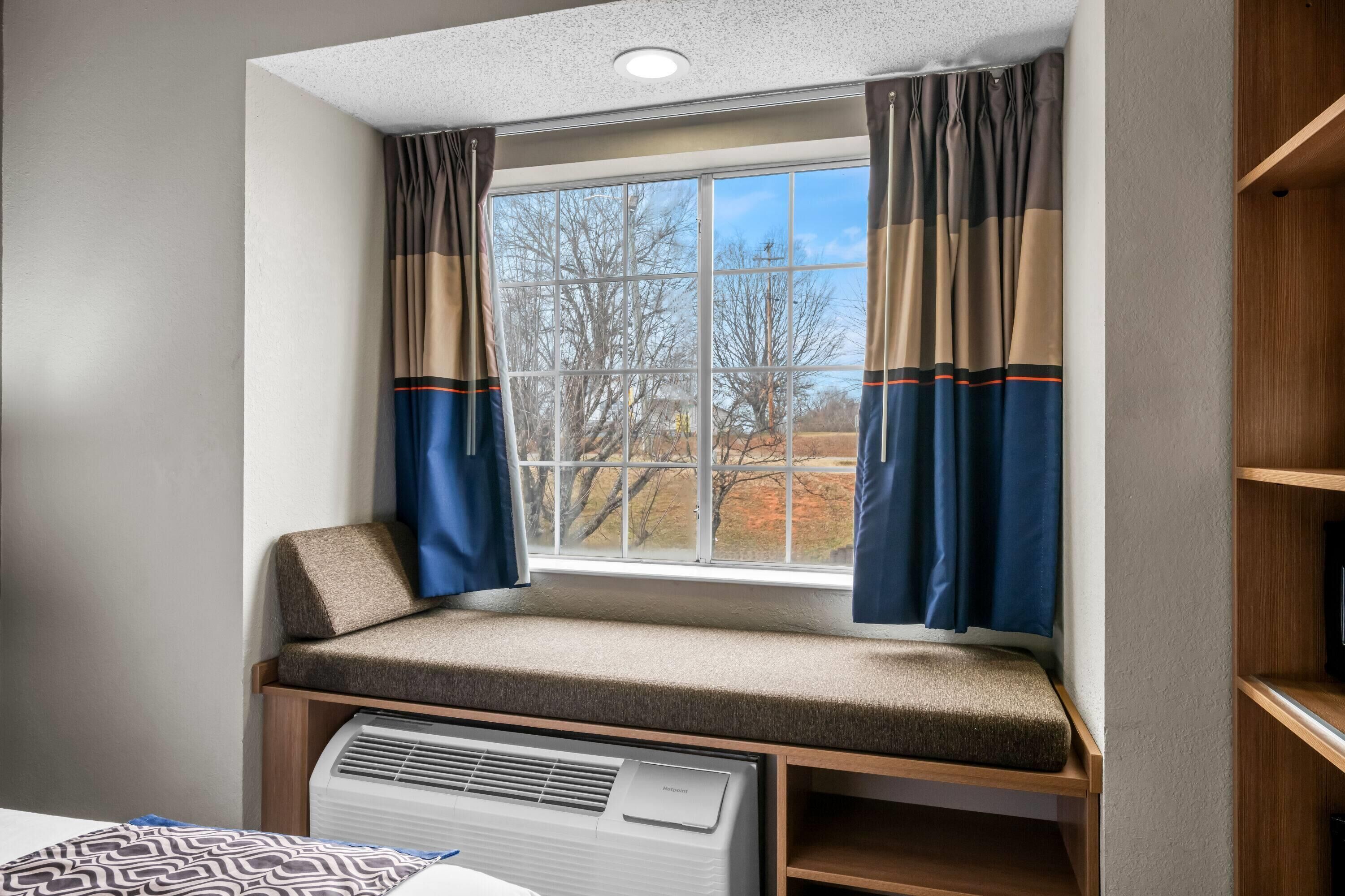 Ein Eckzimmer mit Fenster, einer eingebauten Sitzbank und einem Wandheizkörper.