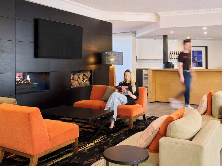 A modern living room with orange sofas, a black coffee table, and a flat-screen TV mounted on the wall.