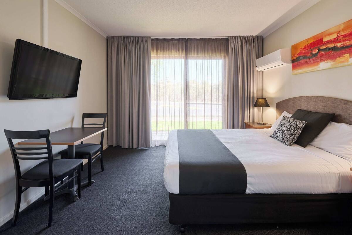 A hotel room with a bed, a desk, a chair, a TV, and a window with curtains.