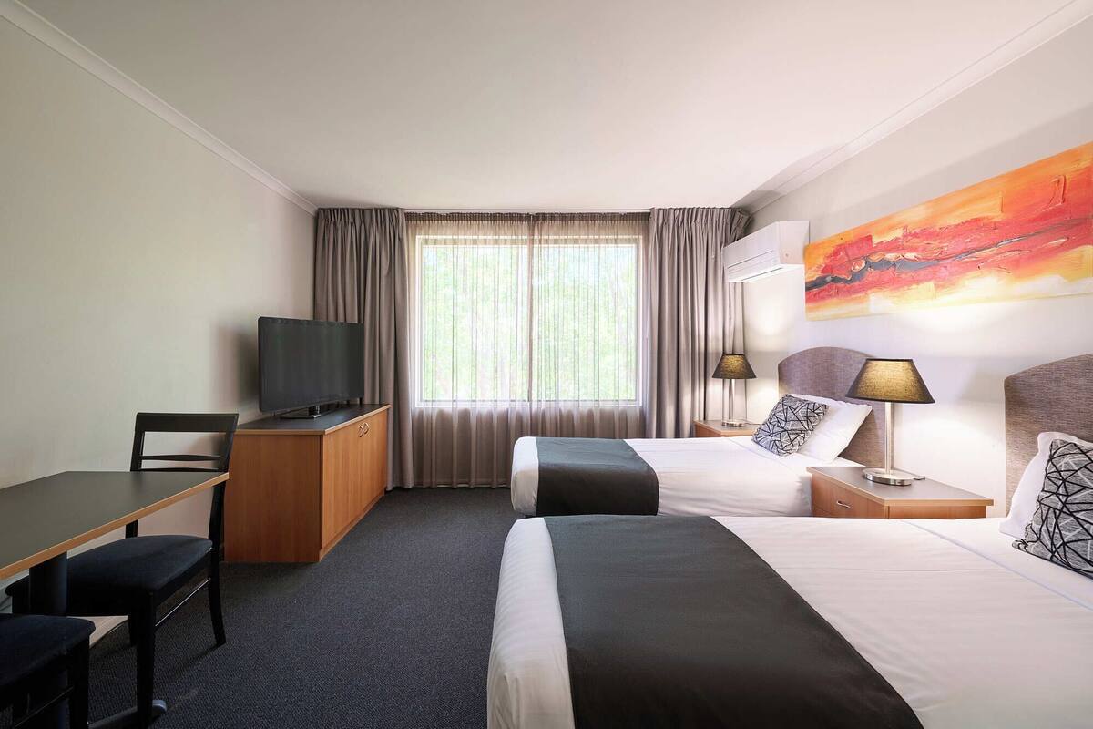 A hotel room with a bed, a desk, a television, and a painting on the wall.