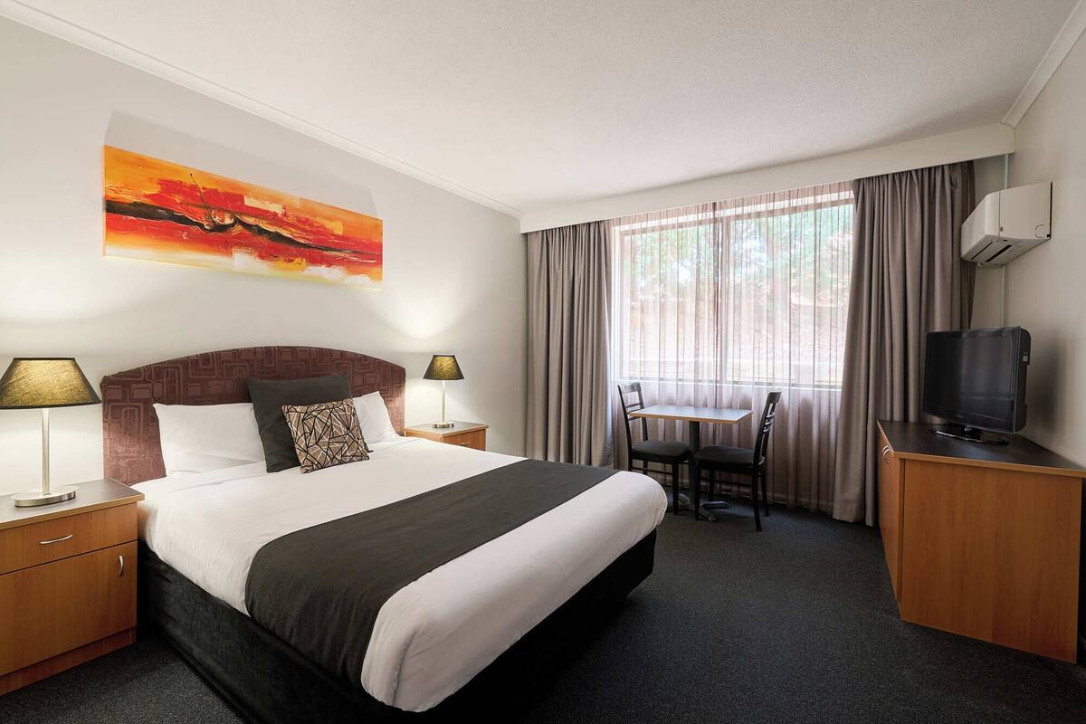 A hotel room with a large bed, a desk with a chair, a television, and a window with curtains.