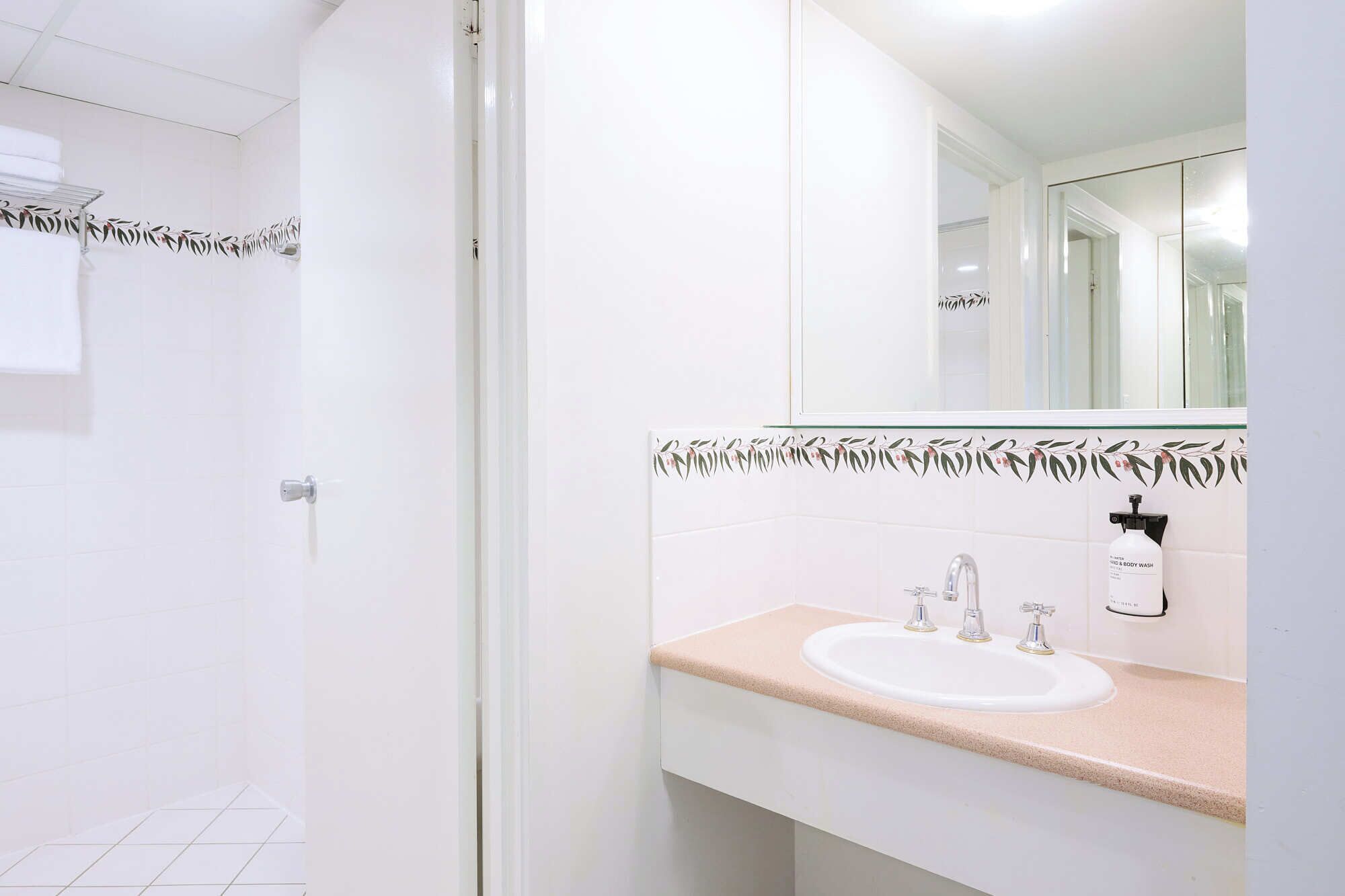 Un baño con lavamanos blanco, un espejo y un perchero para toallas.