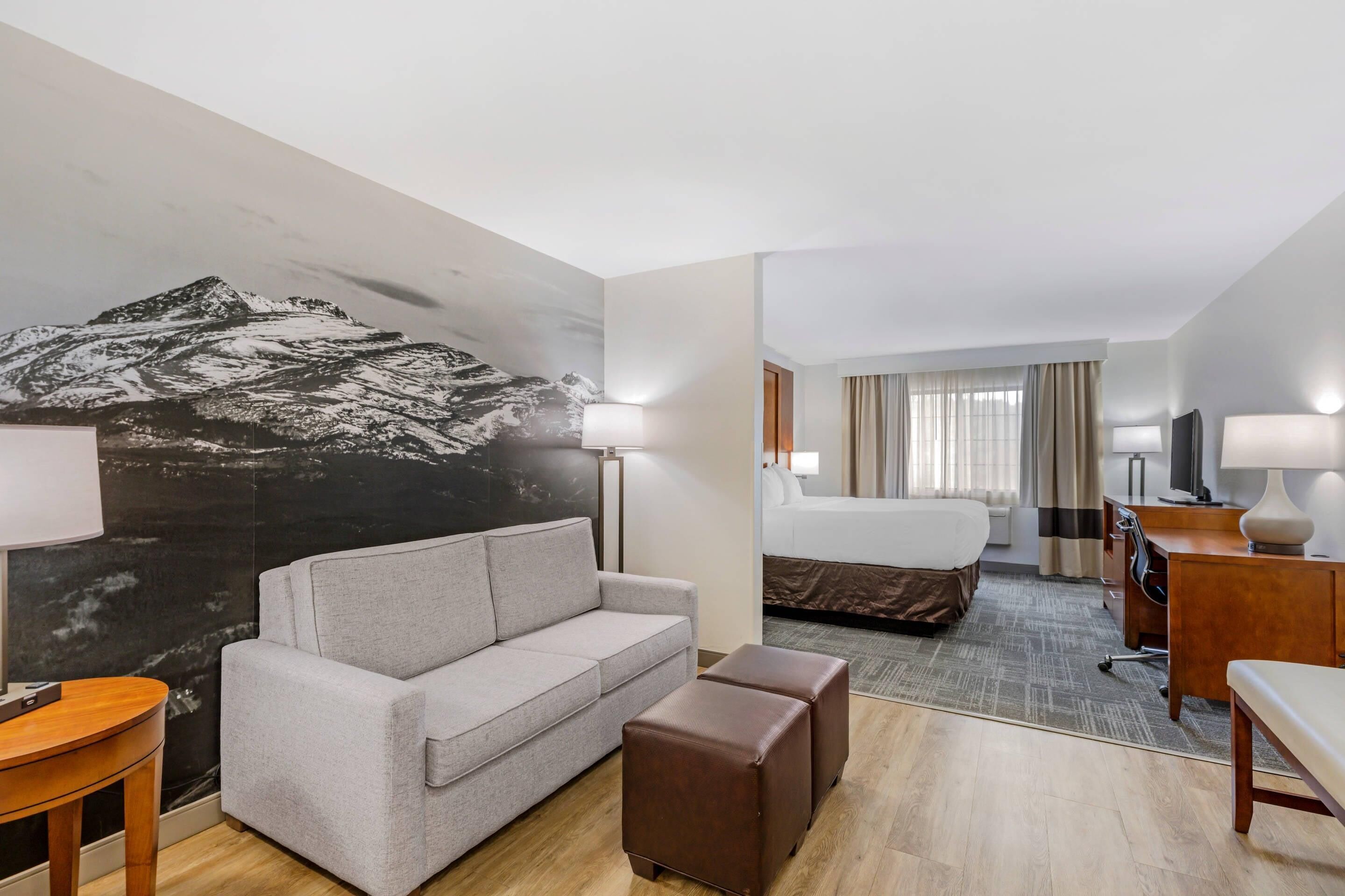 Habitación de hotel con sofá, reposapiés, cama, escritorio, lámpara y un mural grande en la pared.