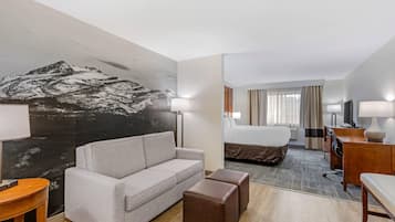 Habitación de hotel con sofá, reposapiés, cama, escritorio, lámpara y un mural grande en la pared.