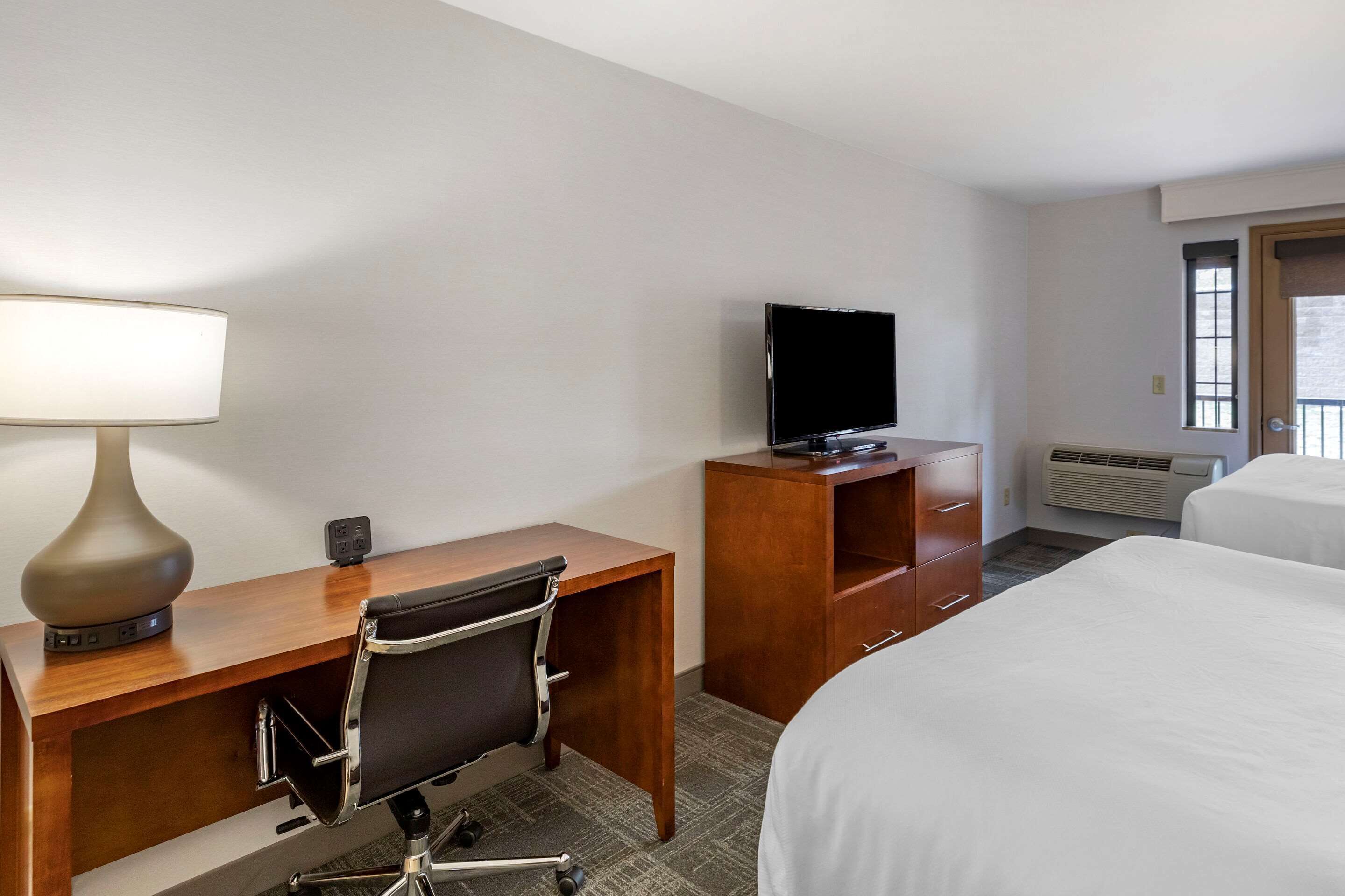A hotel room with a desk, chair, television, and two beds.