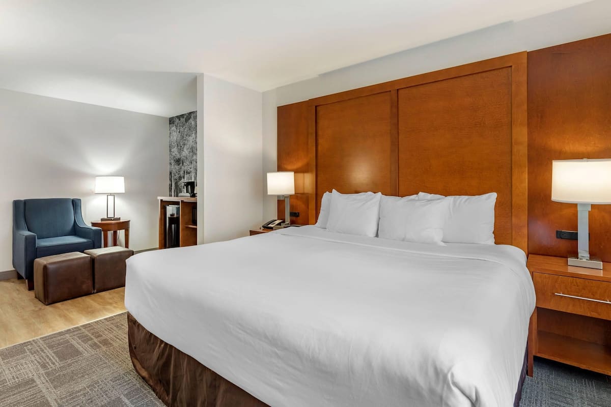 Une chambre d’hôtel avec un grand lit, un fauteuil bleu, deux tables de chevet avec des lampes et une tête de lit en bois.
