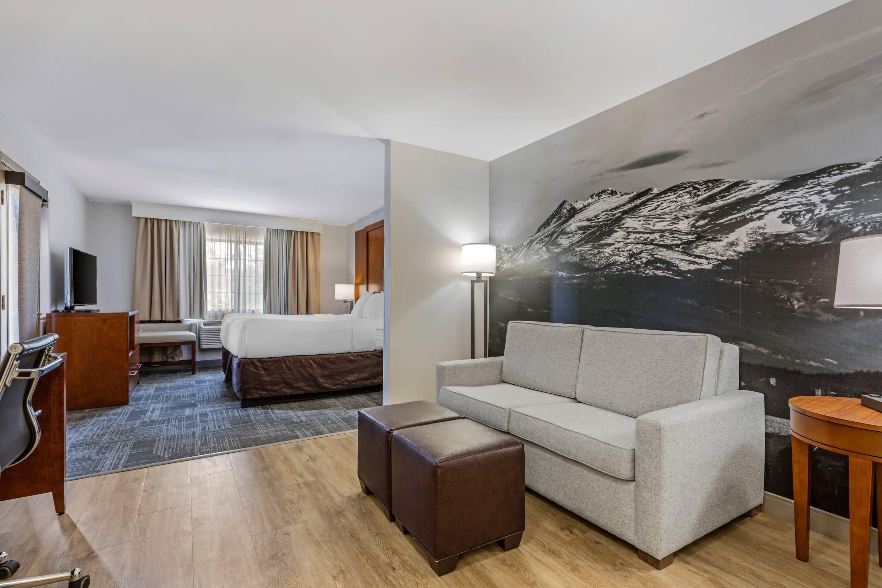 Ein Hotelzimmer mit Bett, einer Couch, einem Schreibtisch, einem Stuhl, einem Fernseher und einem großen Gemälde von einem Berg an der Wand.
