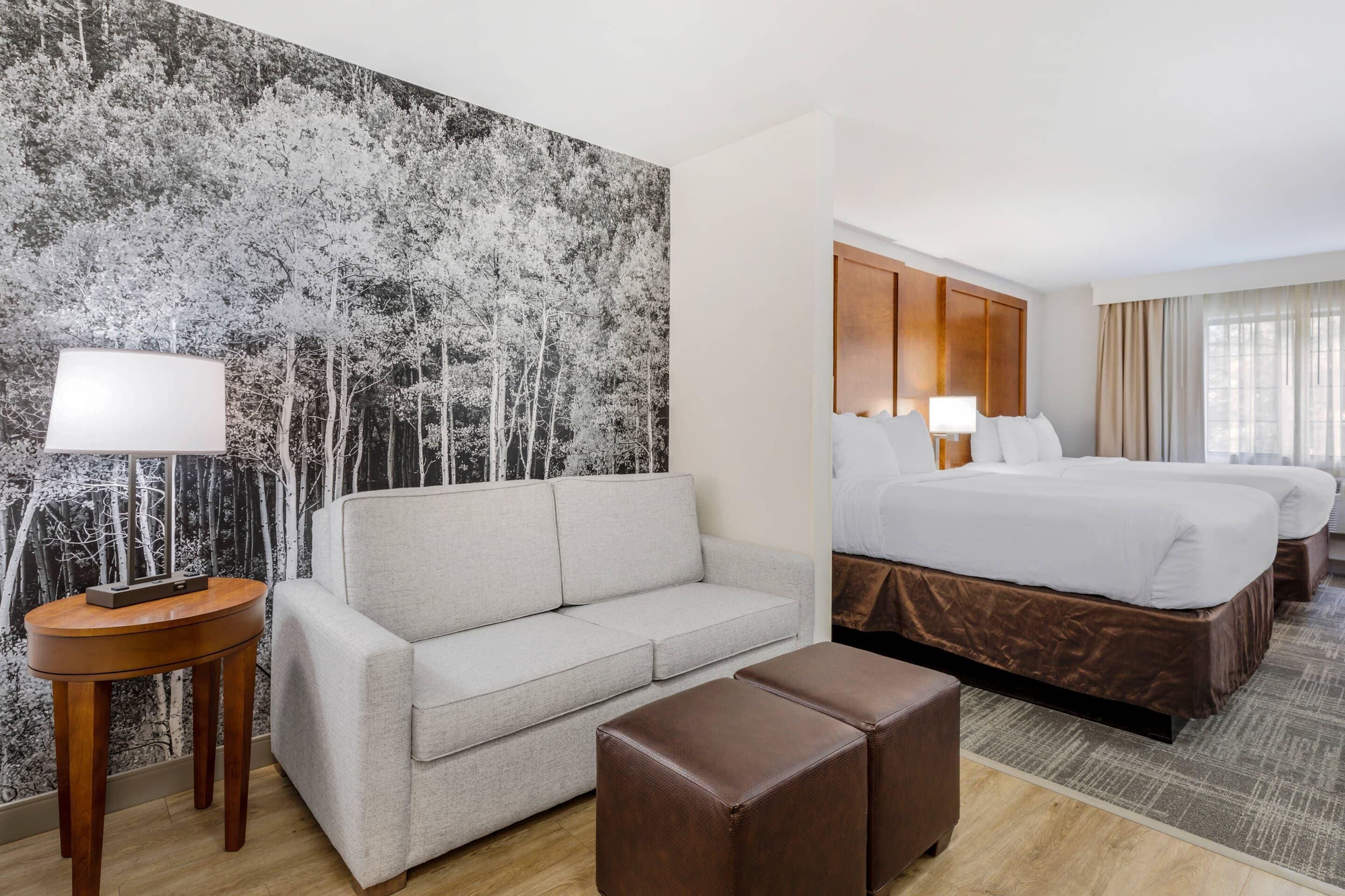 Una camera d'albergo con un letto grande, un divano, un tavolino e un grande murale.