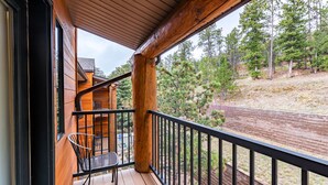 Une terrasse en bois avec une rambarde noire, une chaise et une vue sur une colline boisée.