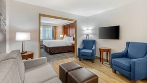 Une chambre d’hôtel avec un lit, deux fauteuils, un canapé, une télévision et une lampe.