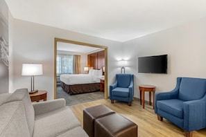 Une chambre d’hôtel avec un lit, deux fauteuils, un canapé, une télévision et une lampe.