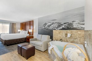 Une chambre d’hôtel avec un lit, un canapé, une baignoire et un grand tableau représentant un paysage de montagne.